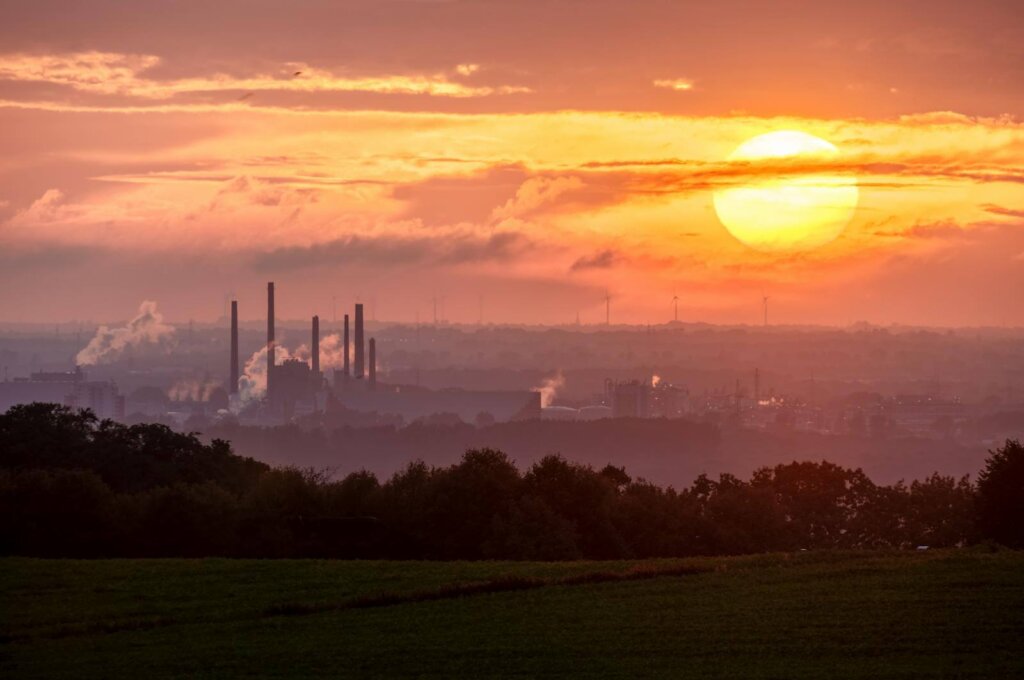 A stunning sunset over an industrial landscape with smoke rising from factory chimneys.