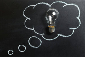 Light bulb laying on chalkboard with drawn thought bubble, symbolizing creative ideas.